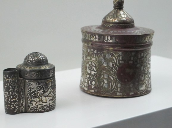 Brass inkwells from Iran, just centimetres high, intricately decorated with a figure on horseback (left) and signs of the zodiac (right) using inlaid silver. The inscription around the top of the one on the right is a blessing.